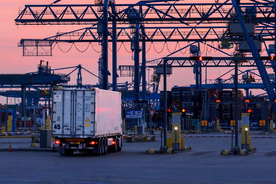 Logistics scene with cranes and a truck at Rotterdam port during sunset. Efficient cargo transportation hub.